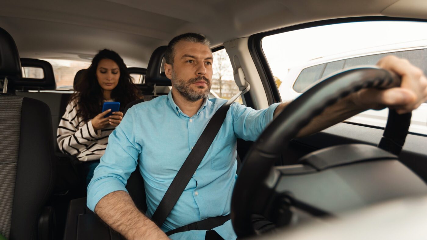 A rideshare driver attentively navigating the road with a passenger in the back.