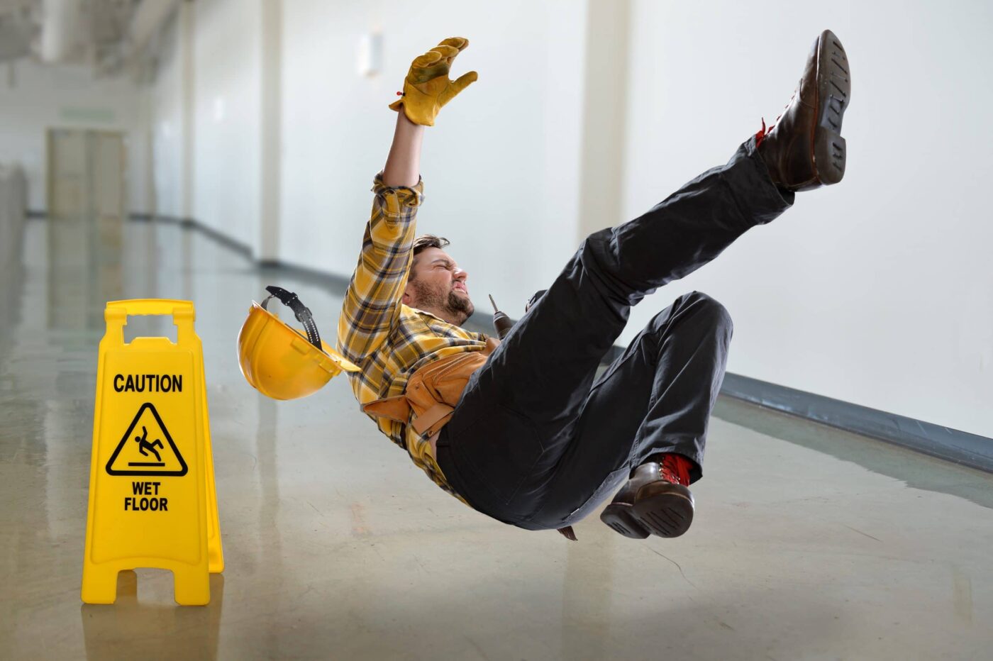 Worker in mid-fall on a shiny floor with a caution sign nearby, illustrating a slip and fall incident.