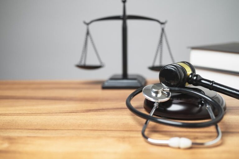 Scales of justice, gavel, and stethoscope on a table, representing medical law and ethics.