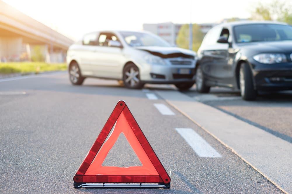 Red warning triangle on the road with two cars in the background after an accident.