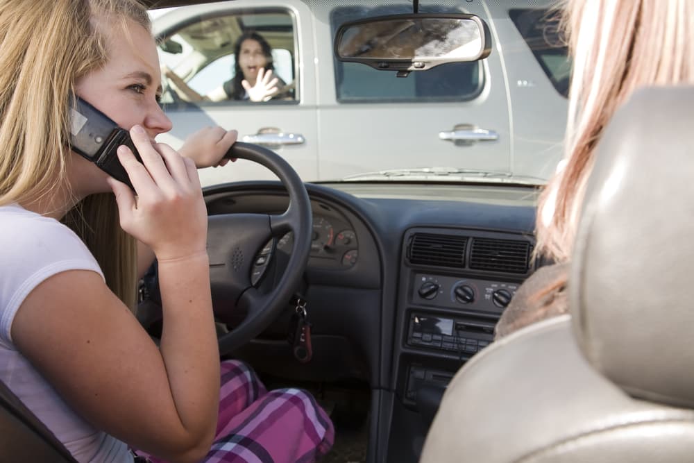 A teenage girl, distracted by her phone, is on the verge of causing a car accident while behind the wheel.
