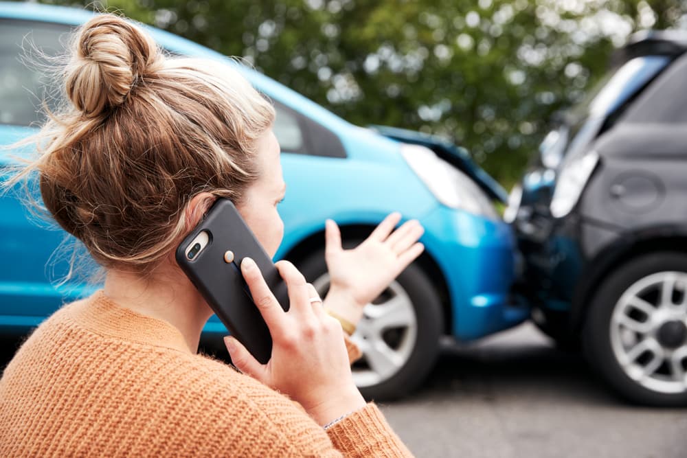 Woman driver in car crash calls insurance or recovery service for assistance.