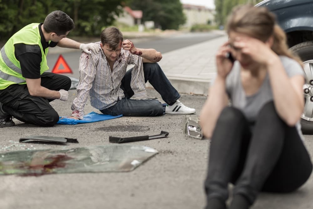 Individuals are seated on the road following a car collision.