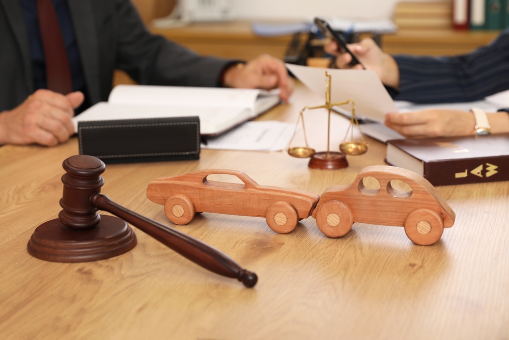 Abogado revisa un caso de accidente automovilístico con modelos de automóviles de madera, mazo y balanzas de justicia en el escritorio.